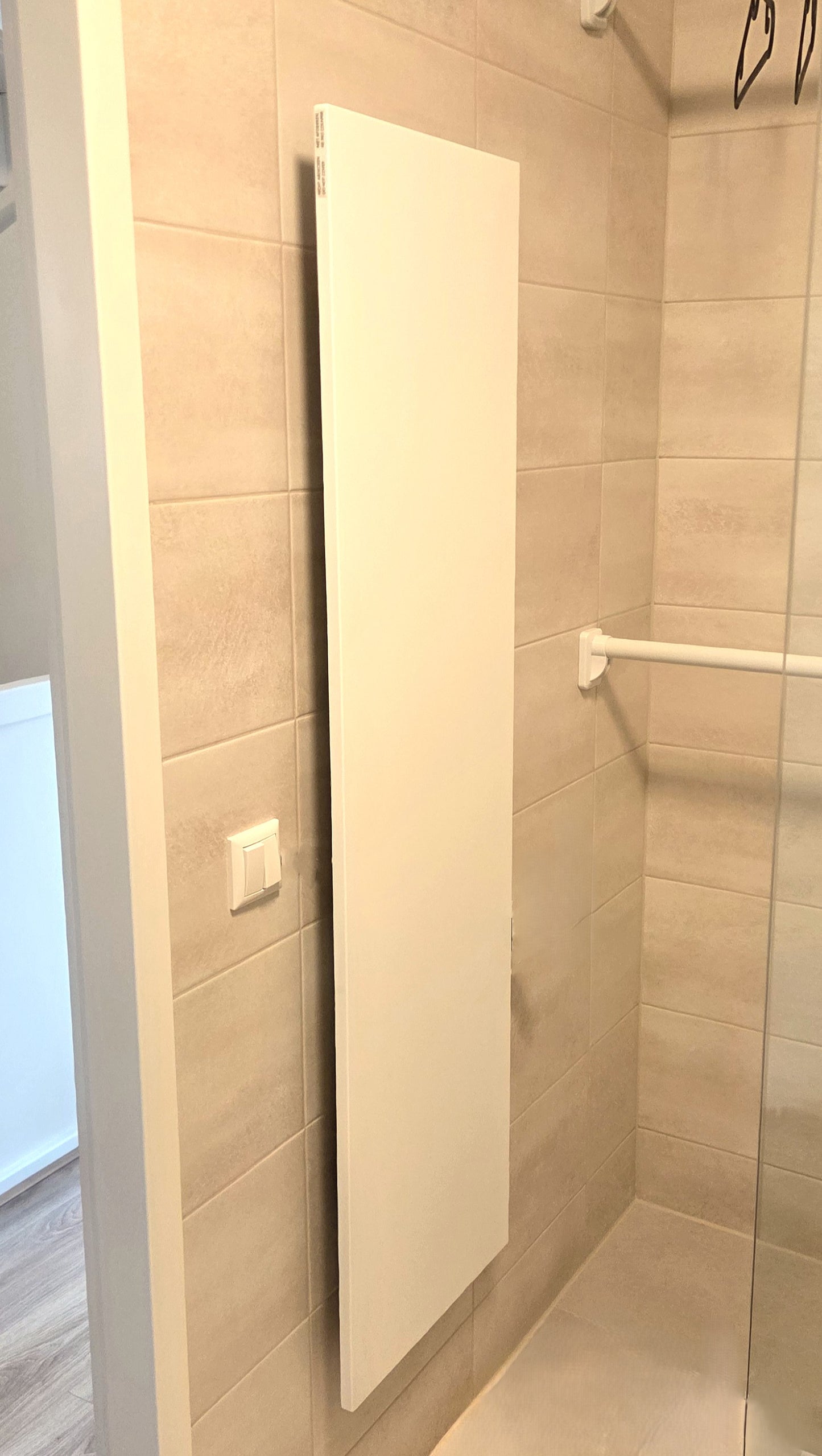 THERON® infrarood verwarmingspaneel verticaal gemonteerd in een stijlvolle badkamer met zandkleurige wandtegels en glazen douchewand